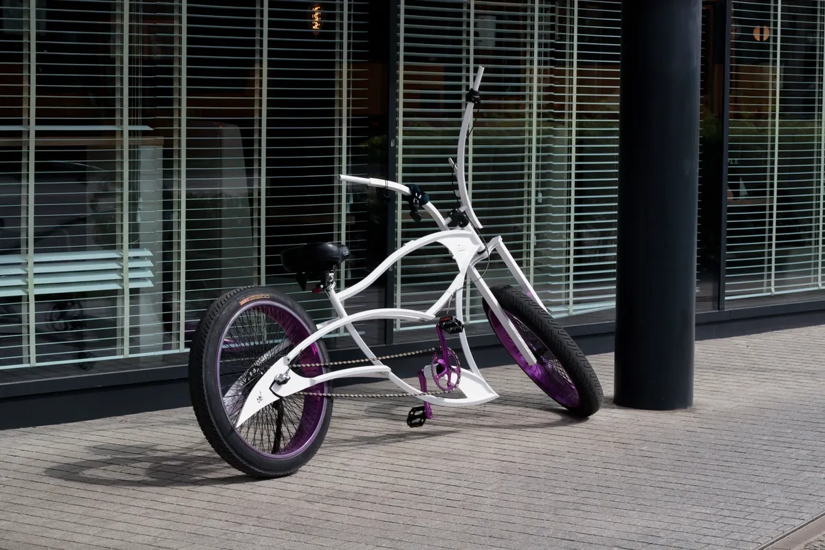 A stylish white bicycle with colorful wheels parked outside a modern glass building.