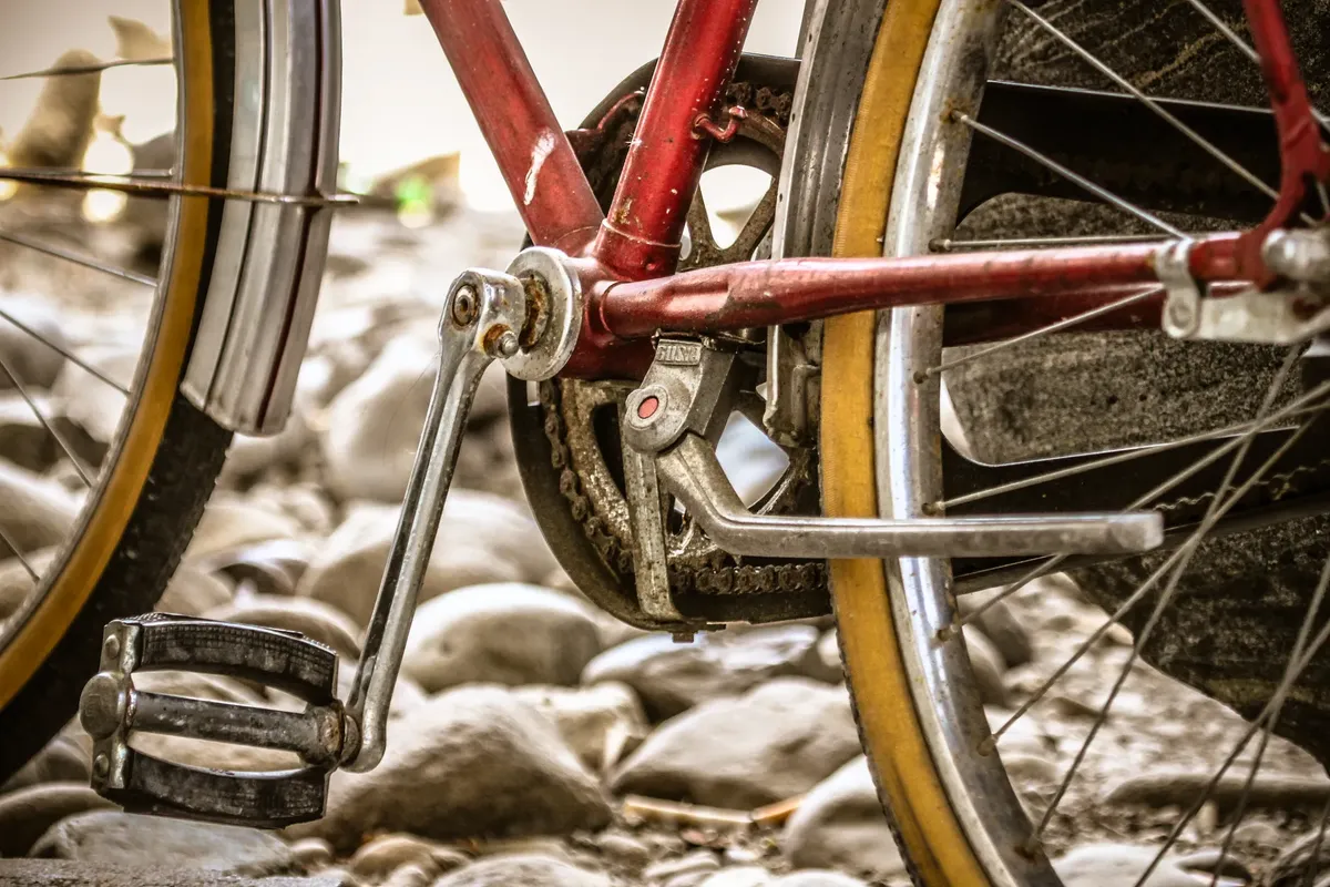 Detailed close-up of a vintage bicycle pedal and chain, parked on pebbles.