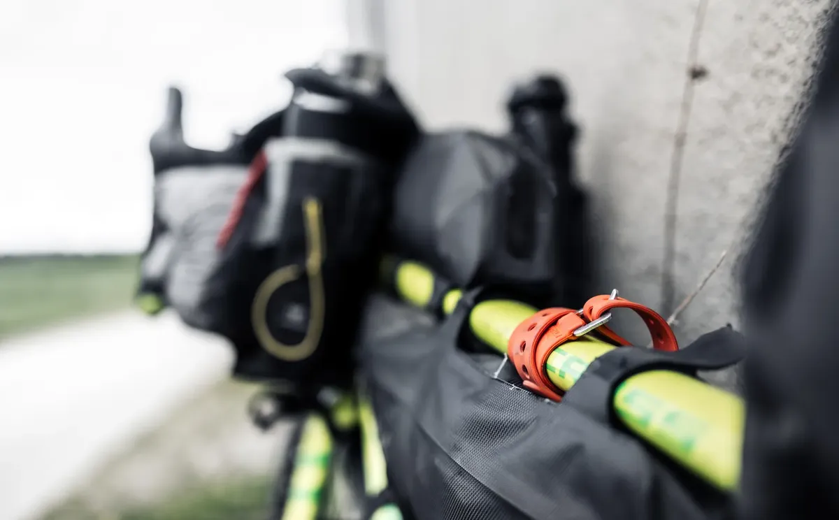 Close-up of packed bicycle gear with focus on a vibrant orange strap and bags attached, ideal for adventure travel.