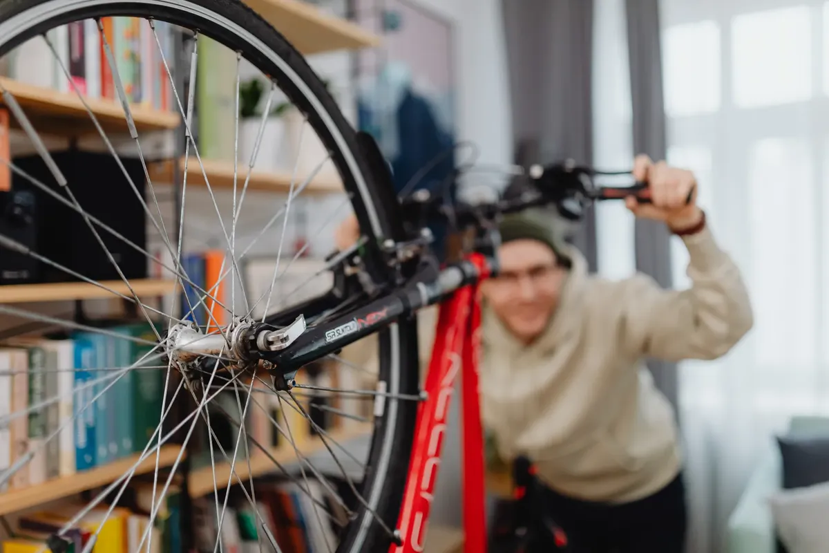 Blurry man in an apartment guiding a bicycle near a bookshelf.