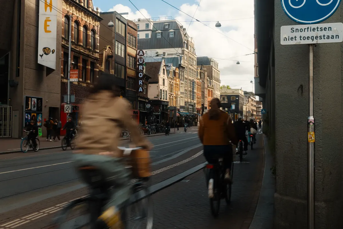 People cycling on a bustling street in Amsterdam with classic architecture and urban atmosphere.