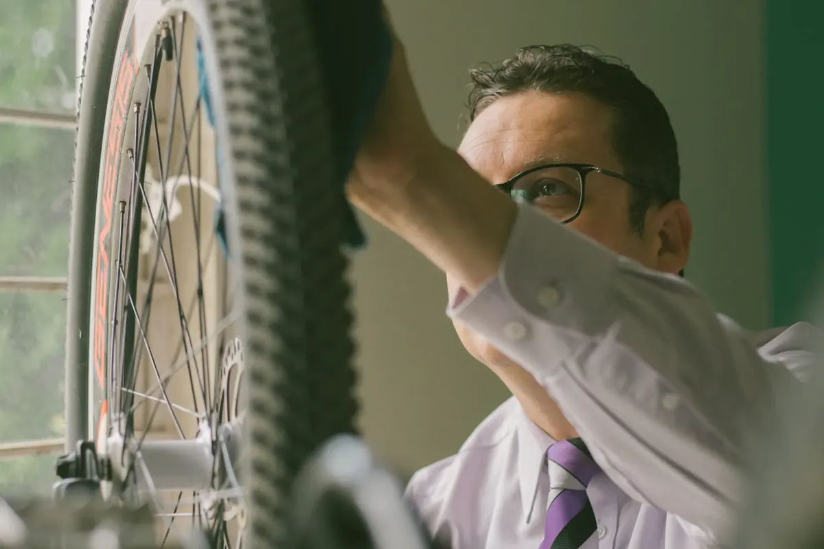 Adult man in a white shirt repairing a bicycle wheel indoors, using a cloth.