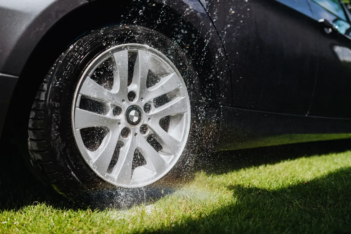 緑の芝の上で車のホイールを水で洗っている動画。